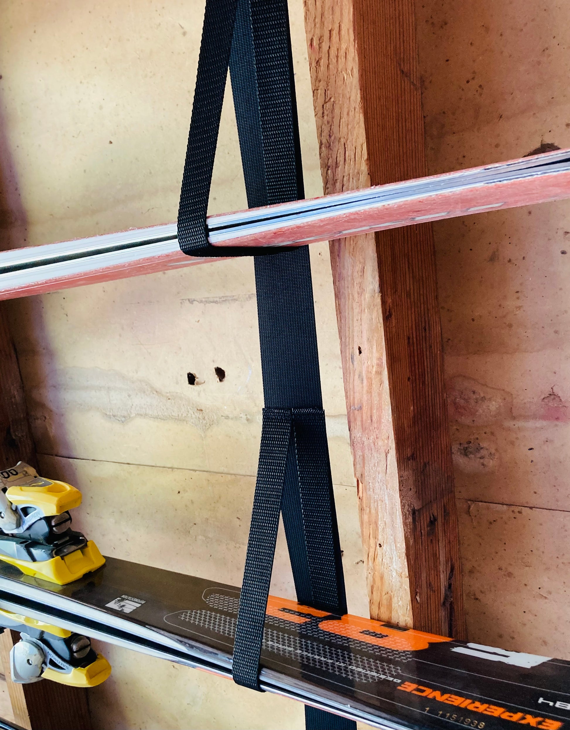 Pair of skis with a strap attached against a wooden wall.
